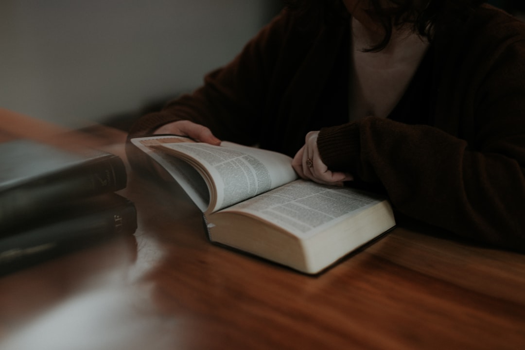 person-reading-book-on-brown-wooden-table-4c-xkkw-rgs